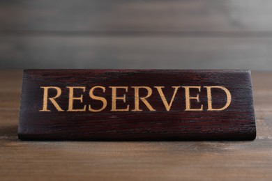 Photo of Elegant sign RESERVED on wooden surface. Table setting element