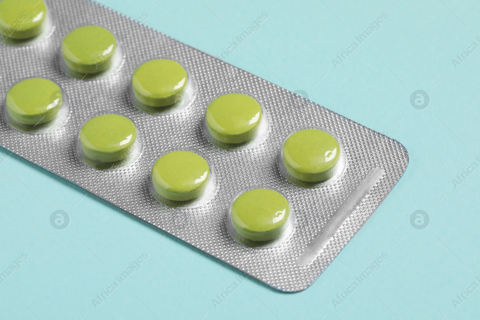 Photo of Green pills in blister on turquoise background, closeup