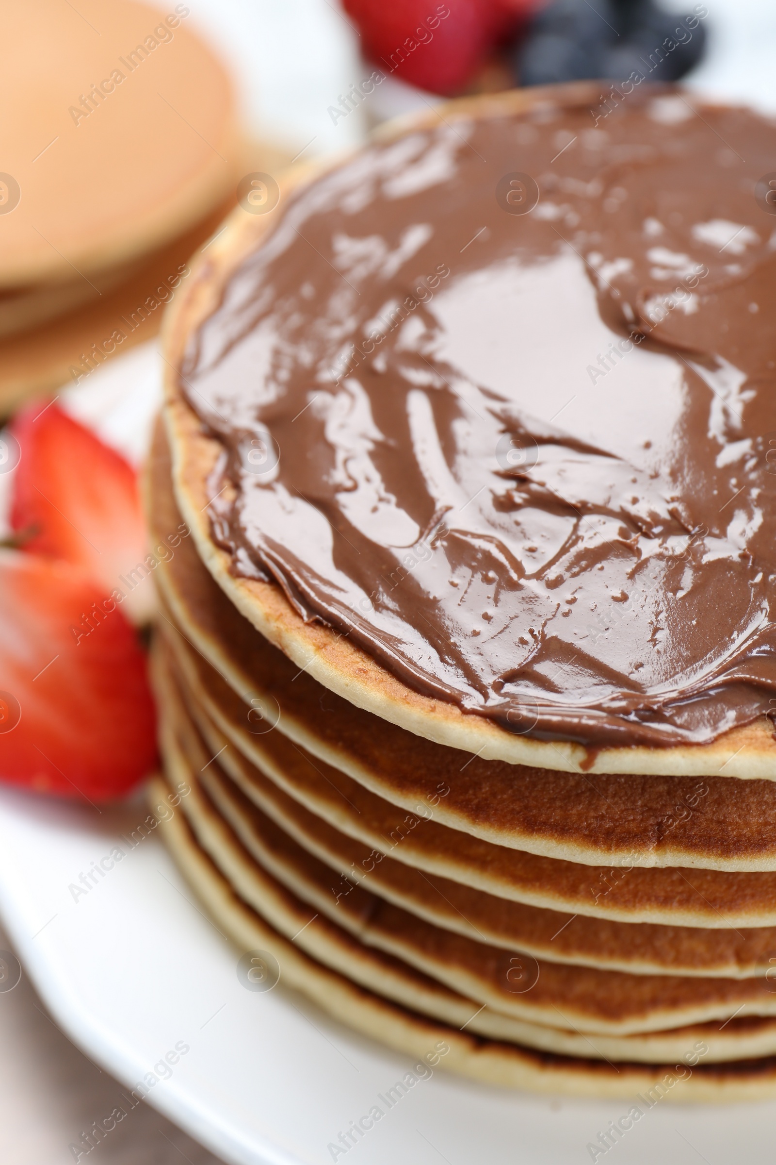 Photo of Tasty pancakes with chocolate paste and strawberries on table, closeup