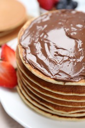 Photo of Tasty pancakes with chocolate paste and strawberries on table, closeup