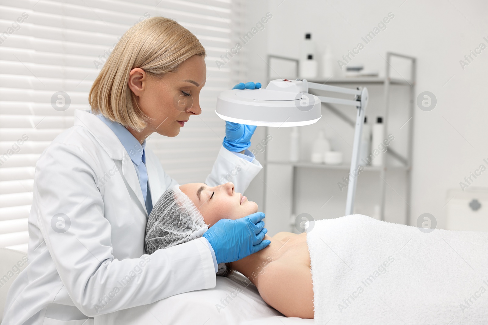 Photo of Dermatologist examining patient`s face under lamp in clinic