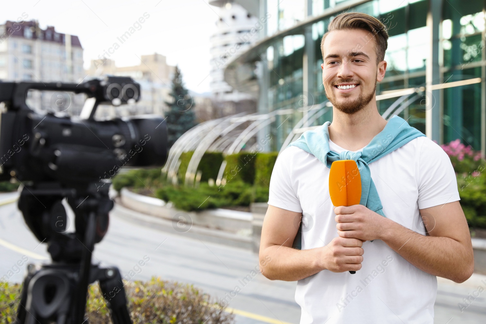 Photo of Young male journalist with microphone working on city street