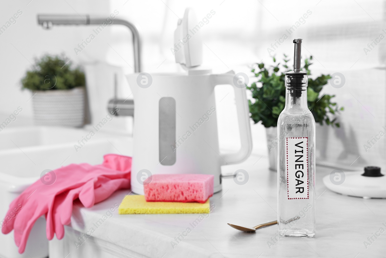 Photo of Cleaning electric kettle. Bottle of vinegar, rubber gloves, sponge and spoon with baking soda on countertop in kitchen