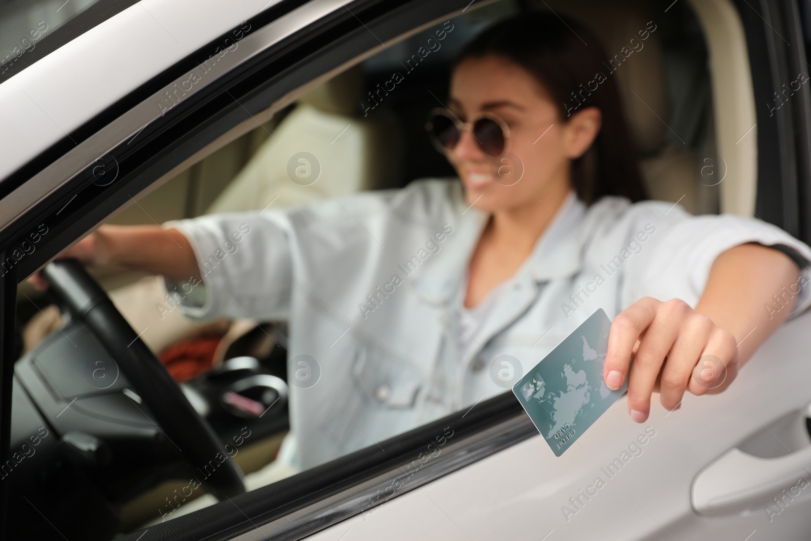 Photo of Woman sitting in car and giving credit card at gas station, focus on hand