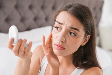 Photo of Young woman with eyelash loss problem looking in mirror indoors