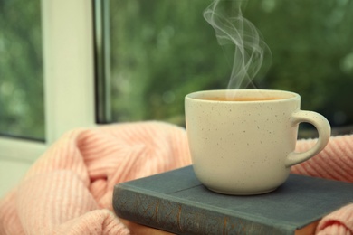 Image of Cup of hot coffee, books and warm sweater on window sill indoors. Space for text