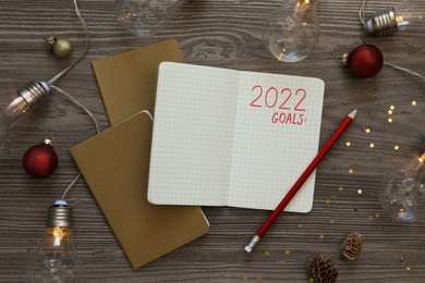 Inscription 2022 Goals written in planner and Christmas decor on wooden background, flat lay. New Year aims