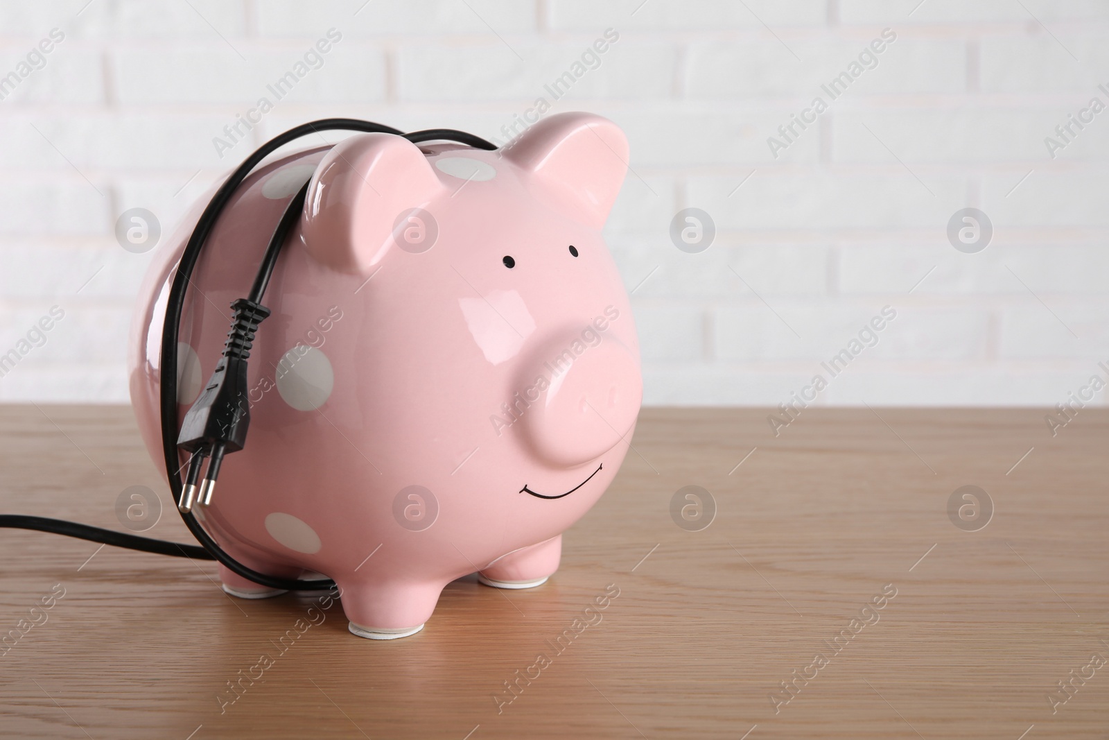 Photo of Piggy bank with power plug on wooden table, space for text. Energy saving concept
