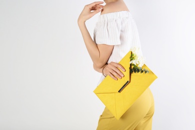 Photo of Stylish woman with clutch and spring flowers against light background, closeup