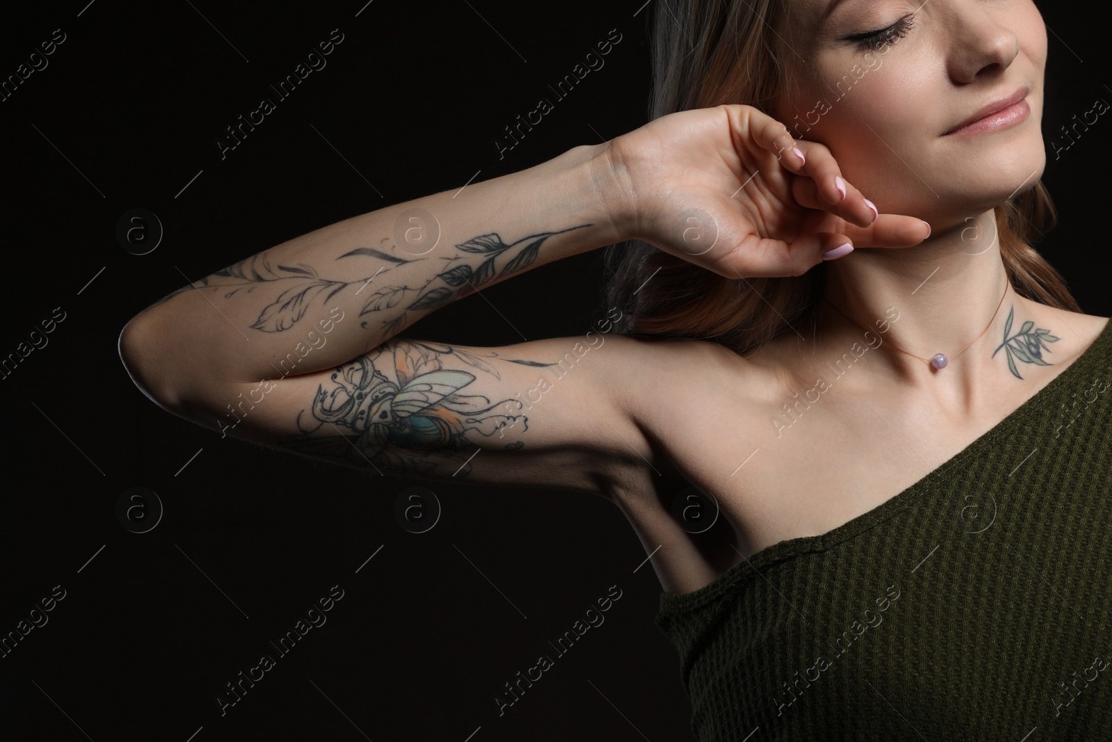 Photo of Beautiful woman with tattoos on body against black background, closeup