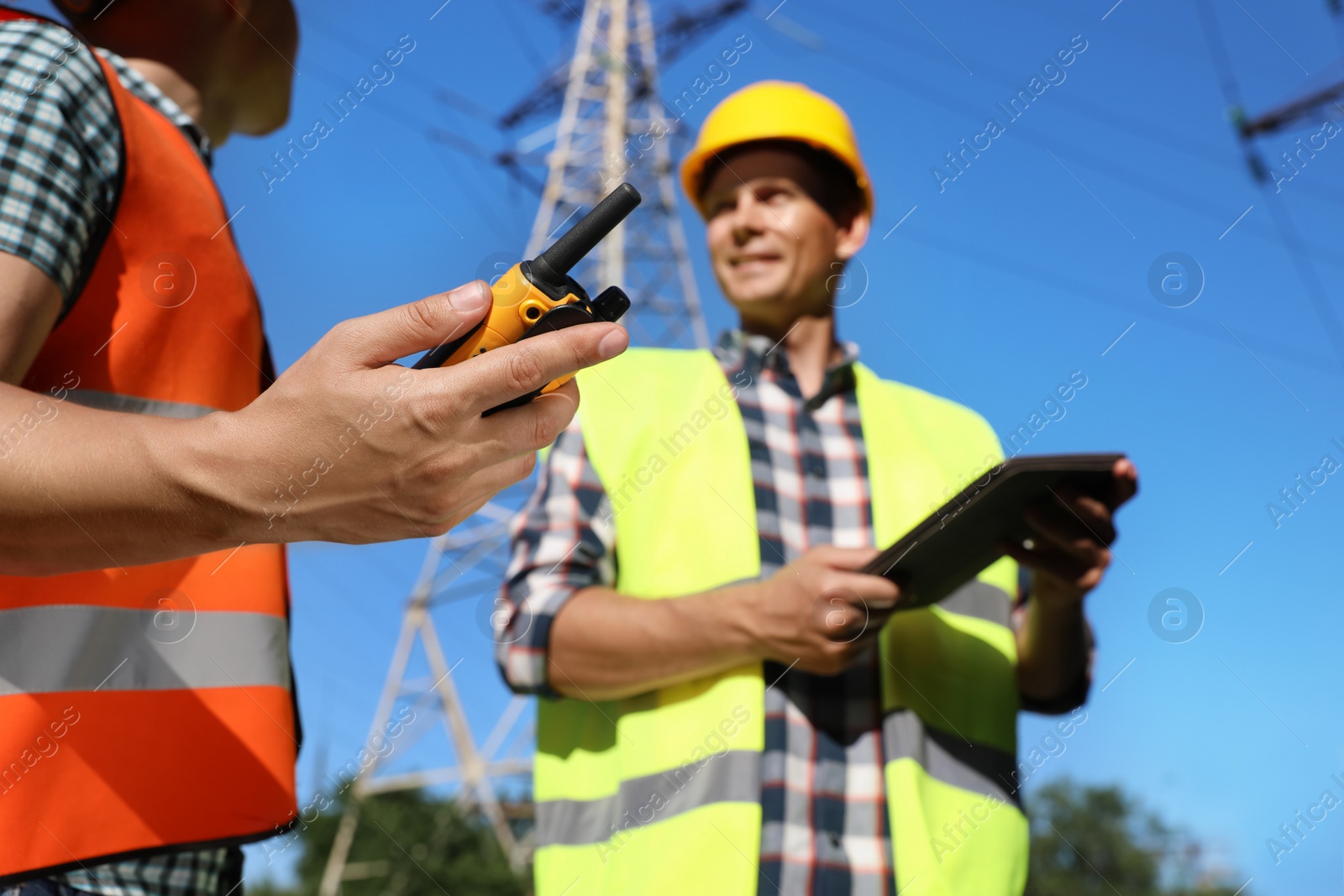 Photo of Professional electricians near high voltage towers, focus on hand with portable radio station