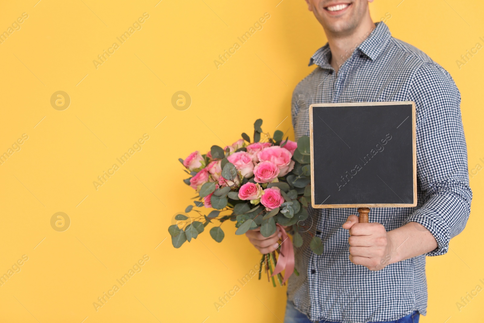 Photo of Male florist holding small chalkboard and bouquet on color background