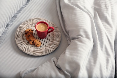 Cup of aromatic coffee and cookies on bed with soft blanket