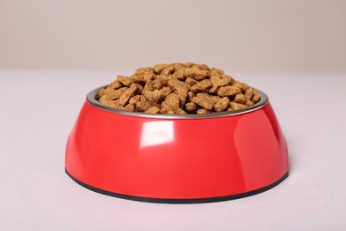 Dry food in red pet bowl on light surface