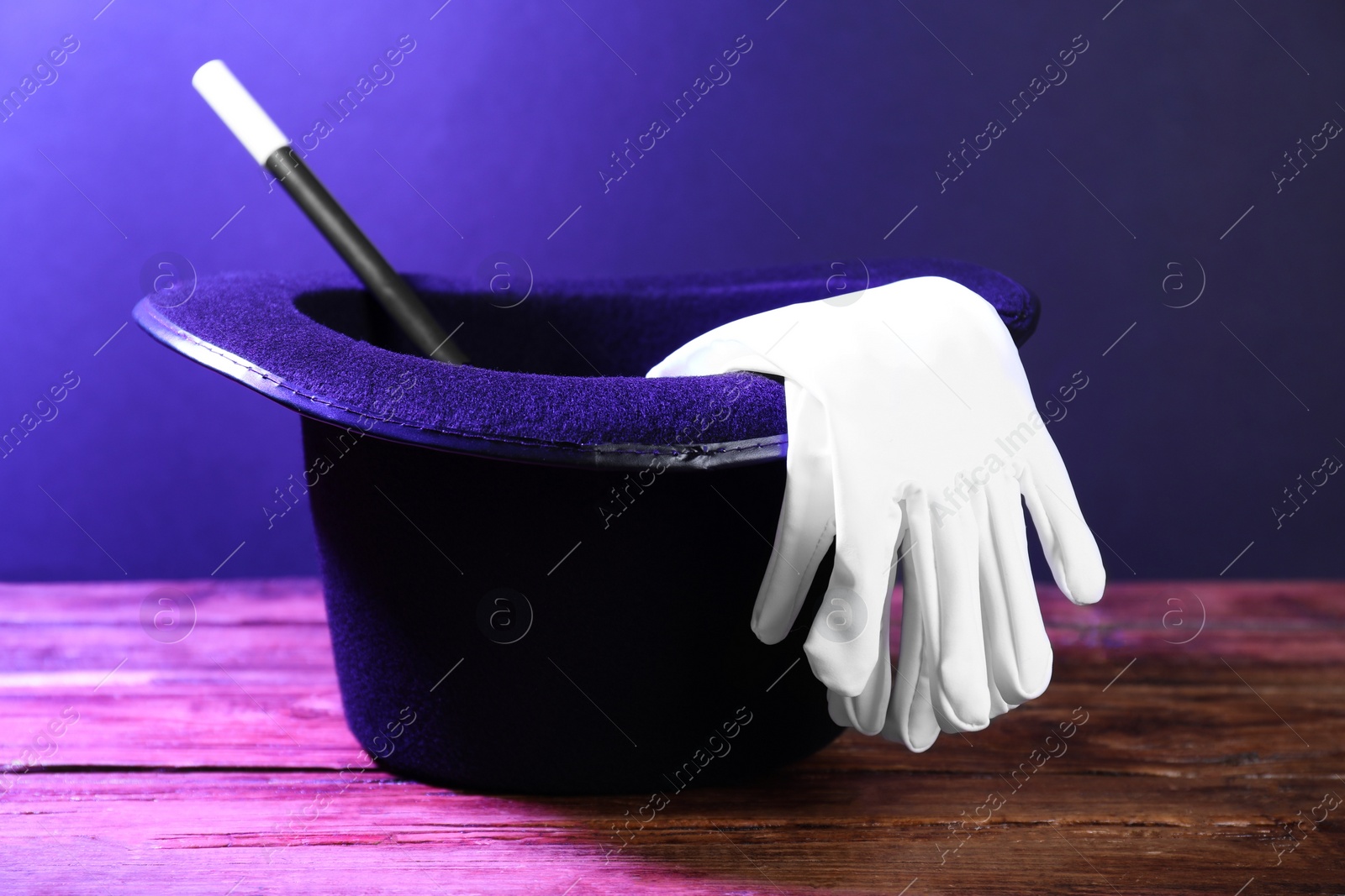 Photo of Black top hat, gloves and wand on wooden table. Magician equipment