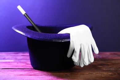 Photo of Black top hat, gloves and wand on wooden table. Magician equipment