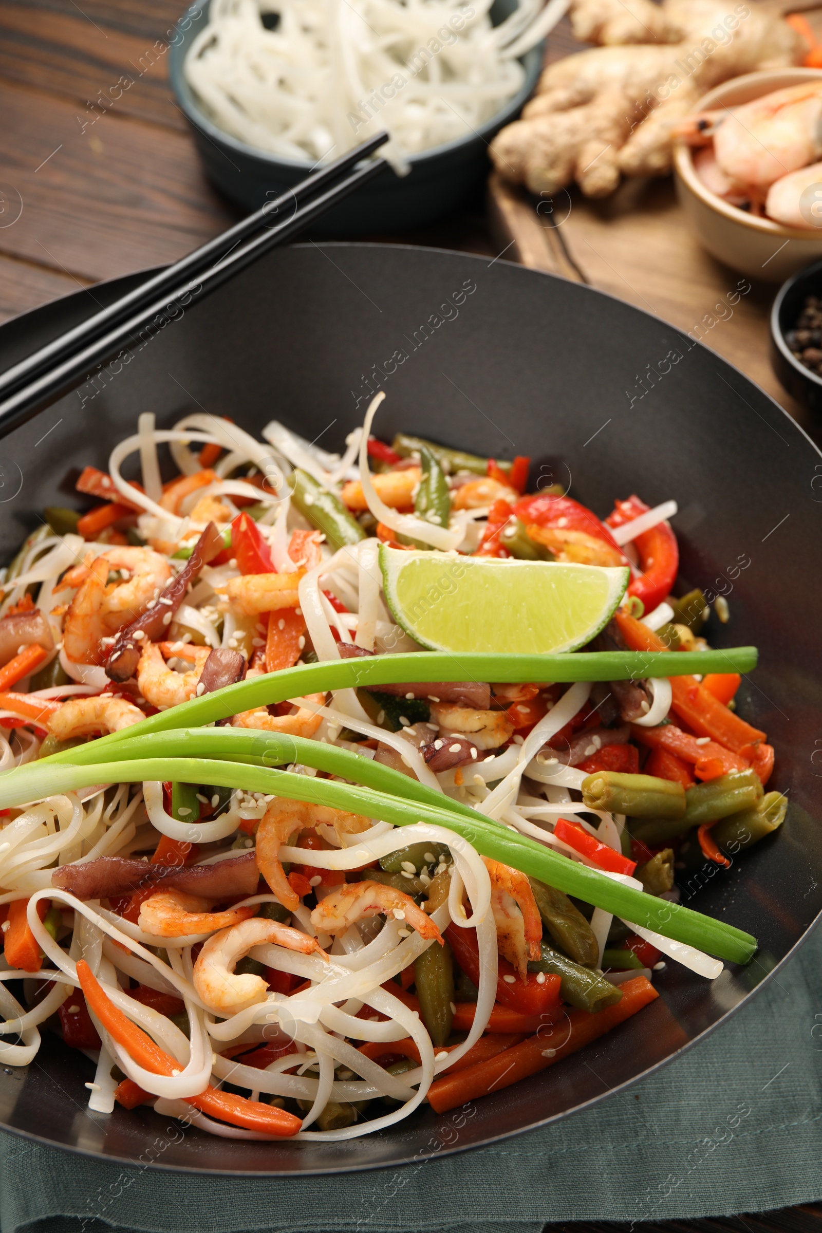 Photo of Shrimp stir fry with noodles and vegetables in wok on table, closeup