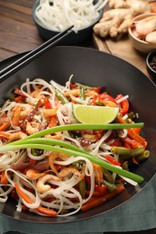 Shrimp stir fry with noodles and vegetables in wok on table, closeup