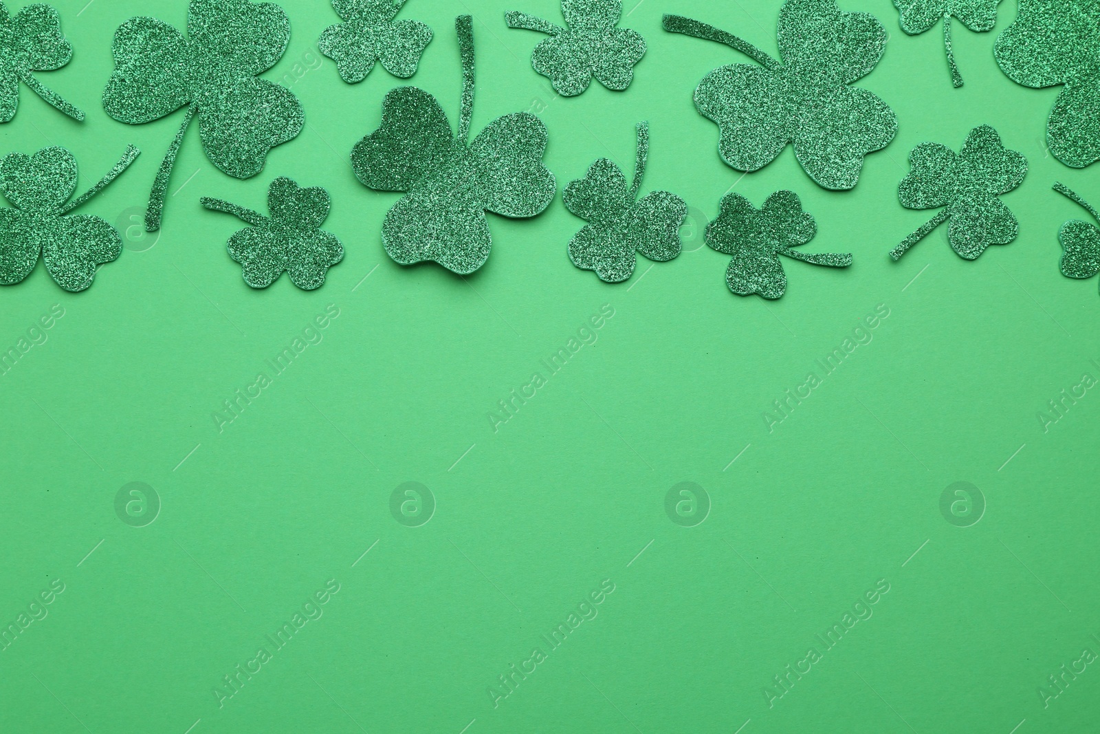 Photo of St. Patrick's day. Shiny decorative clover leaves on green background, flat lay. Space for text