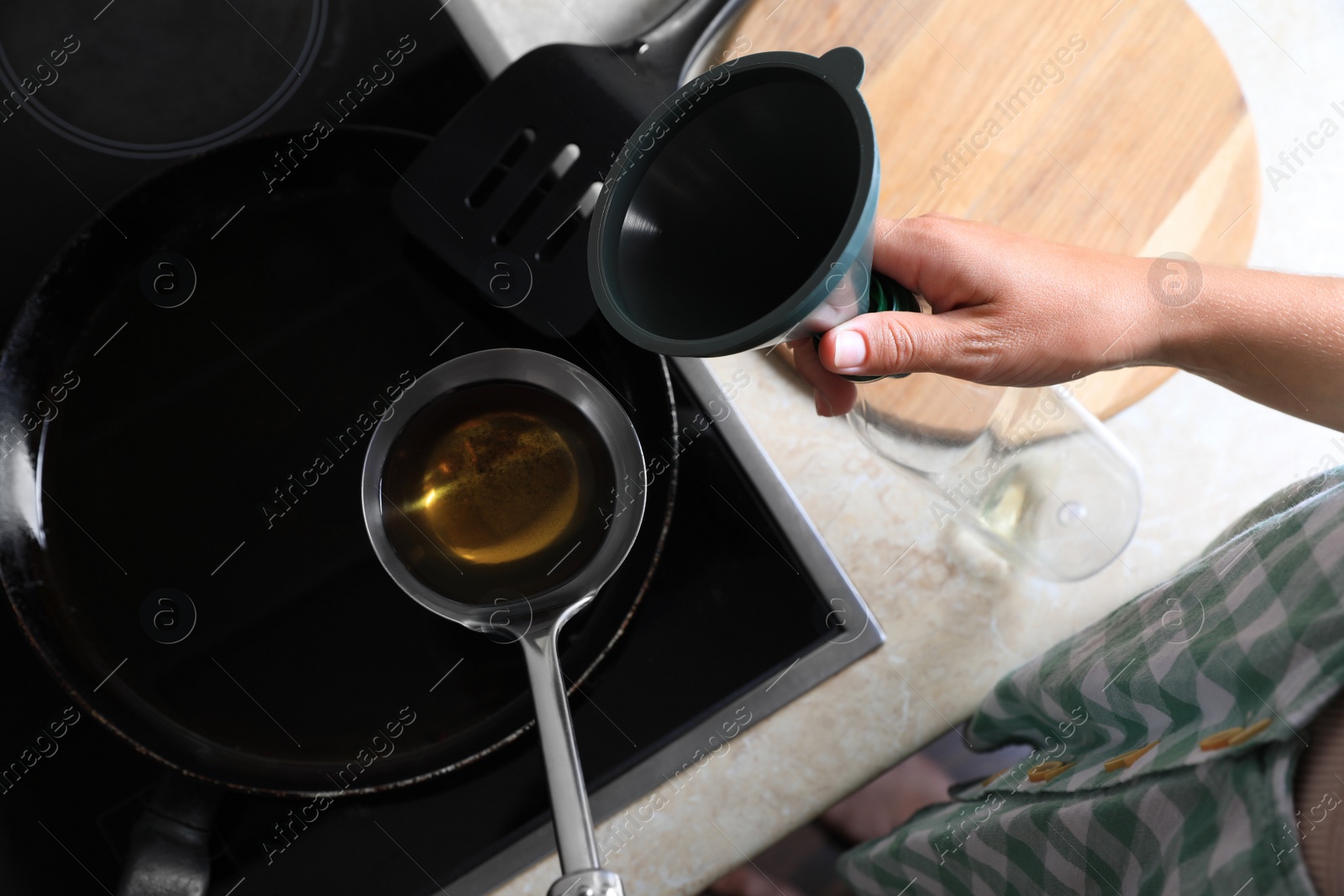 Photo of Woman with used cooking oil, empty bottle and funnel near stove in kitchen, closeup