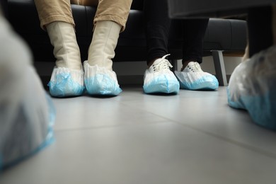 Photo of Women wearing blue shoe covers onto different footwear indoors, closeup