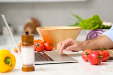 Photo of Man making dinner while watching online cooking course via laptop in kitchen, closeup