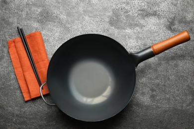 Empty iron wok and chopsticks on dark grey table, flat lay