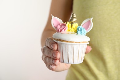 Photo of Woman holding cute sweet unicorn cupcake on white background, closeup. Space for text