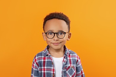 Photo of Cute African-American boy with glasses on orange background