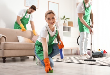 Photo of Woman using sponge and detergent for floor cleaning with her team in living room