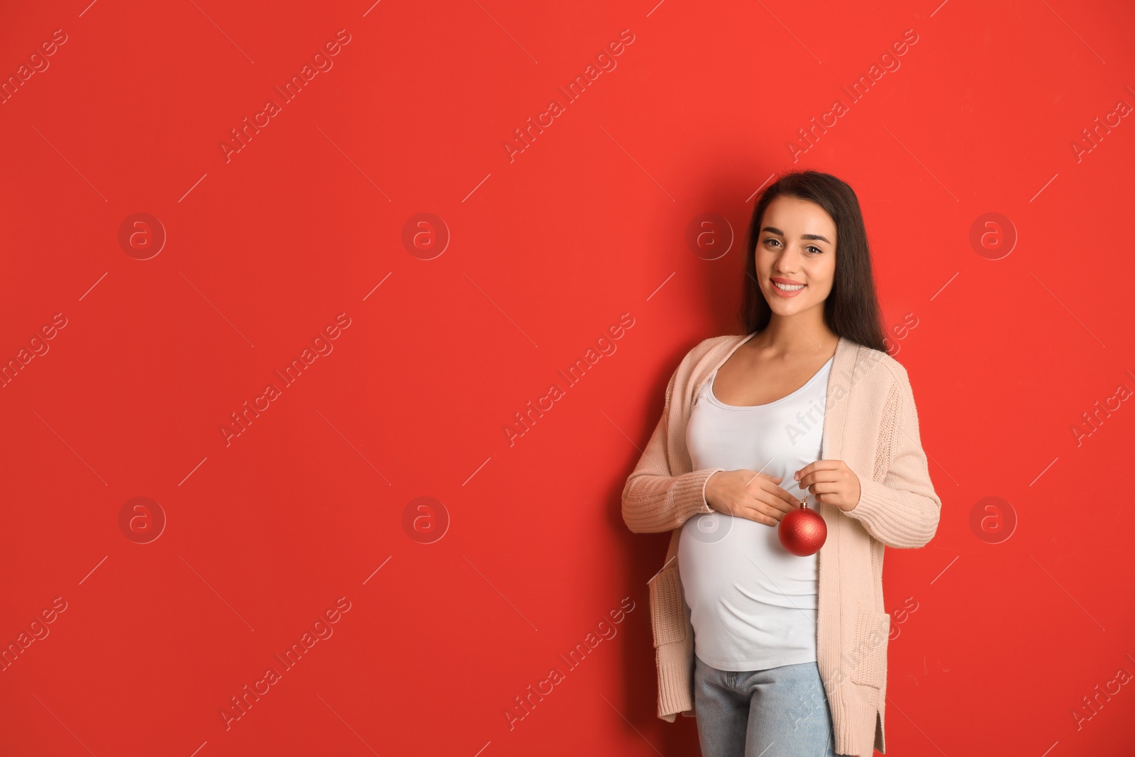 Photo of Happy pregnant woman with Christmas ball on red background, space for text. Expecting baby