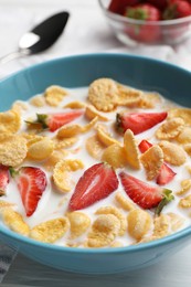 Photo of Bowl of tasty crispy corn flakes with milk and strawberries on white wooden table, closeup