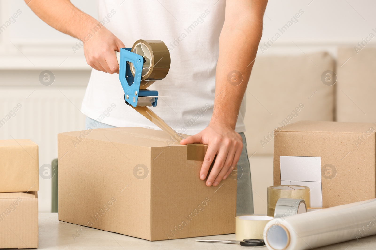 Photo of Man packing box with adhesive tape indoors, closeup