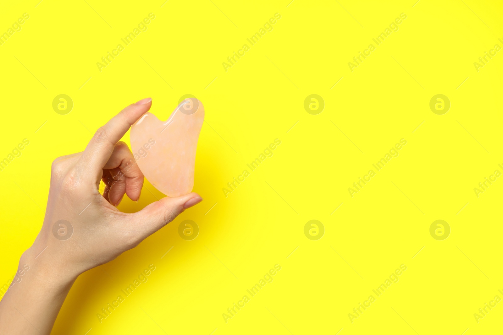 Photo of Woman with rose quartz gua sha tool on yellow background, closeup. Space for text