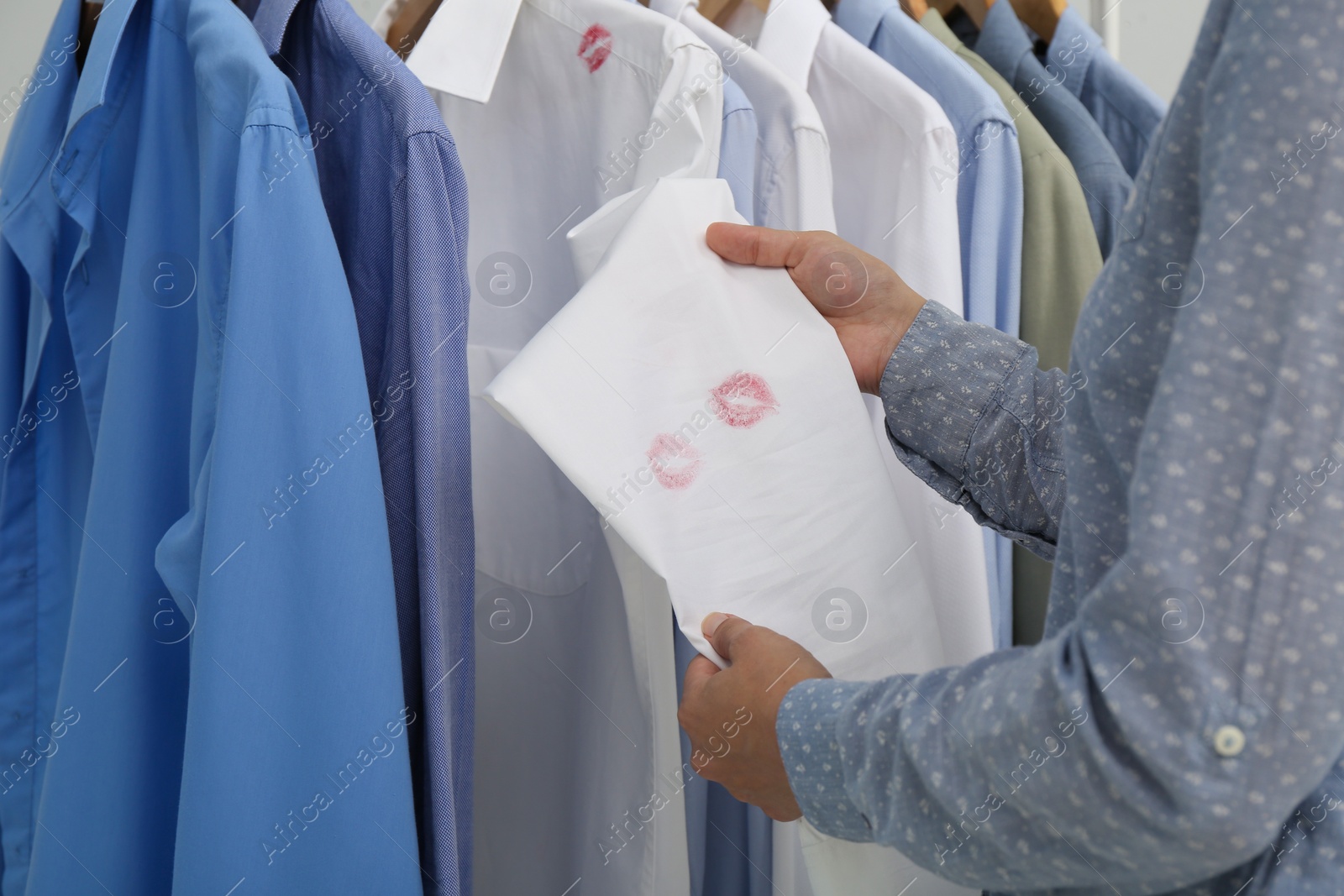 Photo of Woman holding her husband's shirt with lipstick kiss marks near rack, closeup