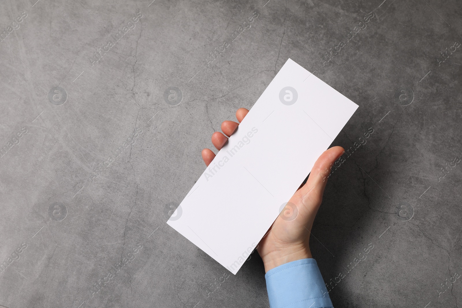 Photo of Woman holding blank card at grey table, top view. Mockup for design