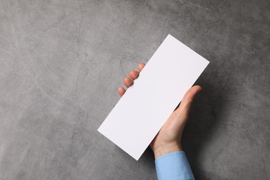 Woman holding blank card at grey table, top view. Mockup for design