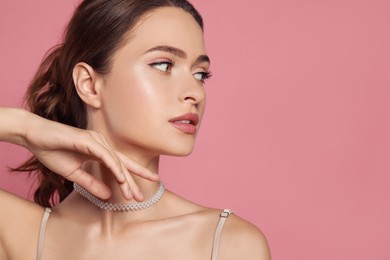 Photo of Young woman wearing elegant pearl necklace on pink background, space for text