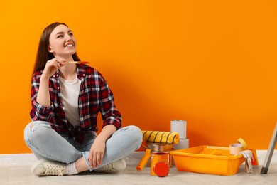 Photo of Happy designer with brush and painting equipment near freshly painted orange wall, space for text