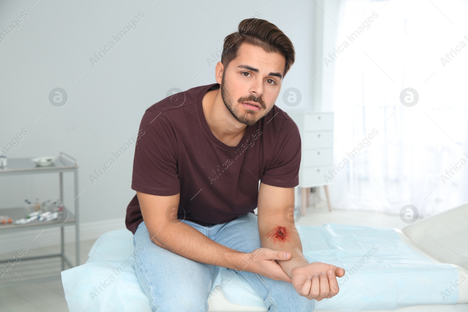 Photo of Young man with injured arm in clinic. First aid