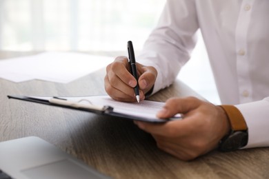 Photo of Businessman signing document at table indoors, closeup