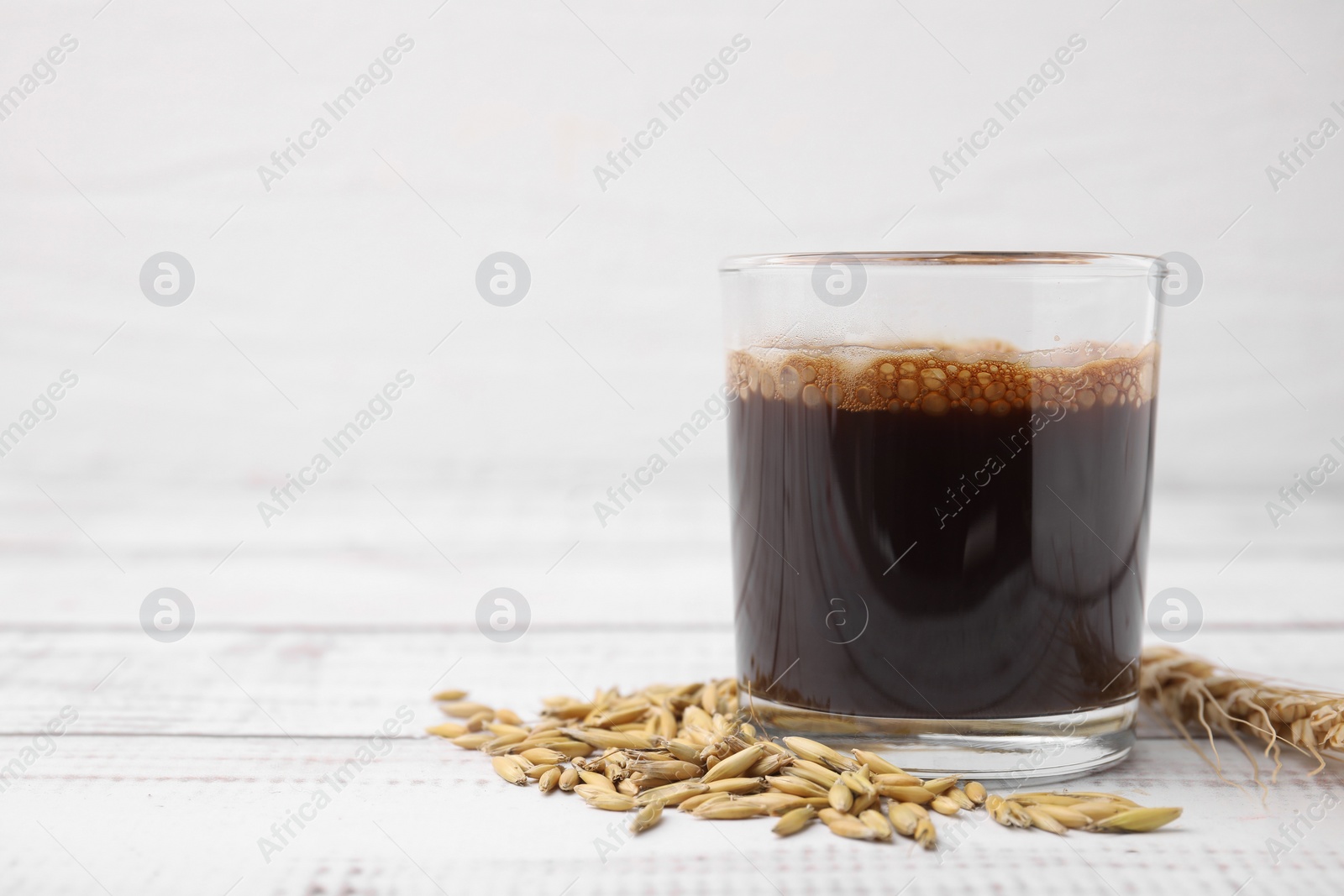 Photo of Cup of barley coffee, grains and spike on white wooden table, closeup. Space for text