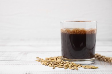 Photo of Cup of barley coffee, grains and spike on white wooden table, closeup. Space for text