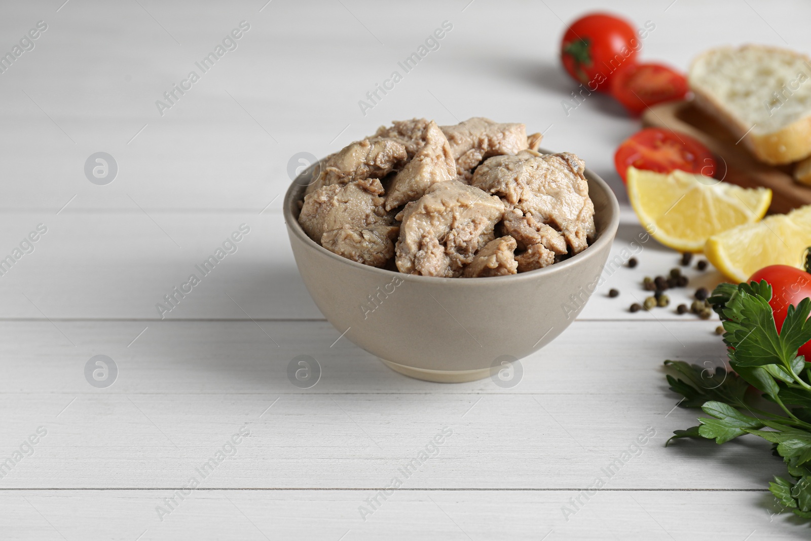 Photo of Bowl of tasty cod liver and different products on white wooden table. Space for text