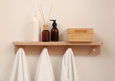 Photo of Wooden shelf with towels, soap dispensers and aromatic reed freshener on beige wall. Interior element