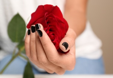 Woman with black manicure holding rose, closeup. Nail polish trends