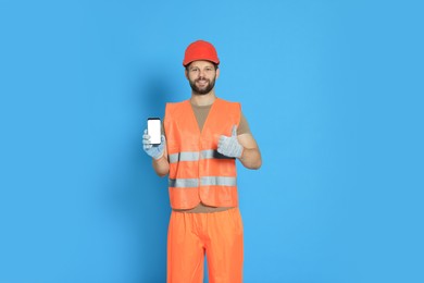 Photo of Man in reflective uniform showing smartphone and thumbs up on light blue background