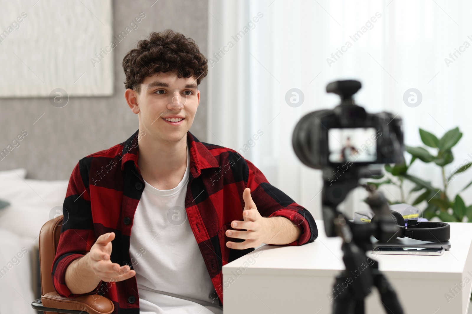 Photo of Smiling teenage blogger explaining something while streaming at home