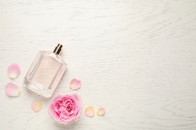 Photo of Flat lay composition with bottle of perfume and rose on white wooden background, space for text