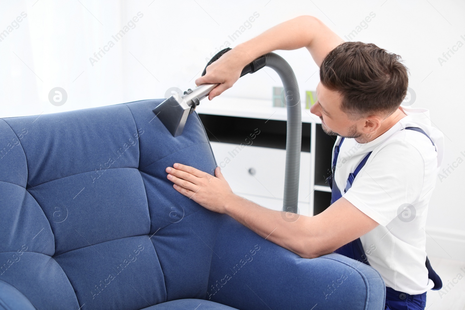 Photo of Dry cleaning worker removing dirt from armchair indoors